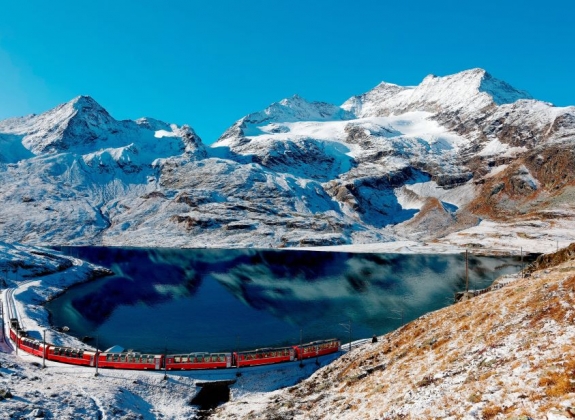 bernina express passing by a lake and snowy mountain