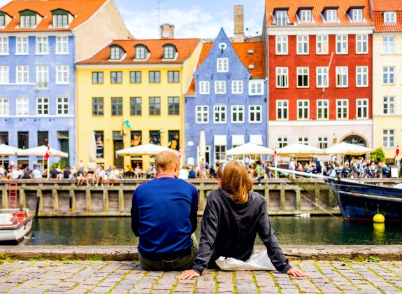 Tourists enjoying the scenic summer view of Nyhavn pier. Colorful building facades with boats and yachts in the Old Town of Copenhagen, Denmark