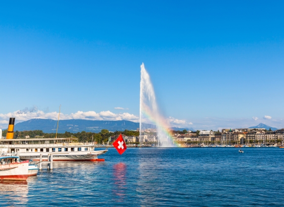 Beautiful view of the water jet fountain with rainbow in the lake of Geneva and the cityscape of Geneva at sunset, Switzerland