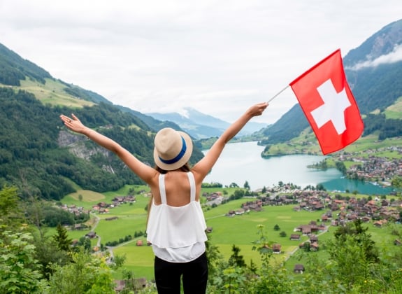 Young woman with swiss flag enjoying great landscape view on the valley with lake and village in Switzerland.