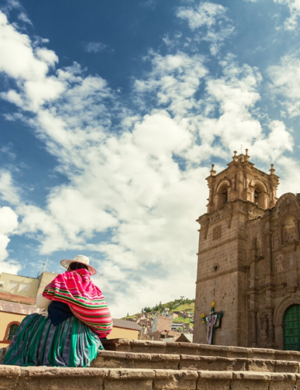 Woman with keperina (bag on her back) sitting on the steps of the Cathedral of Puno (Peru)