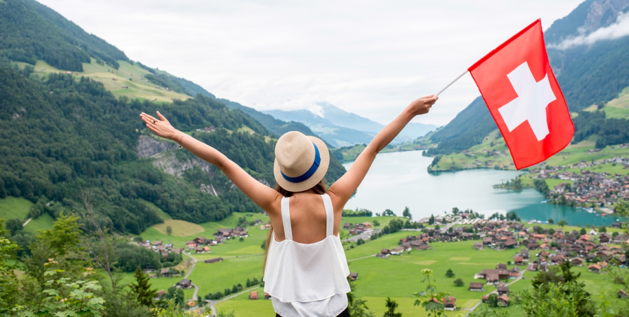 Young woman with swiss flag enjoying great landscape view on the valley with lake and village in Switzerland.
