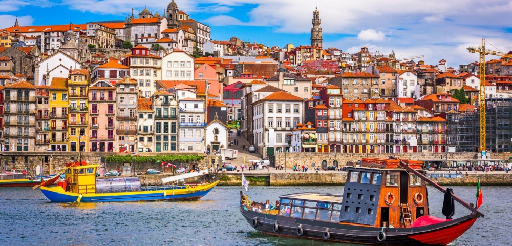 Wooden tour boats cruise the river in Porto, Portugal with the colorful city skyline in the background