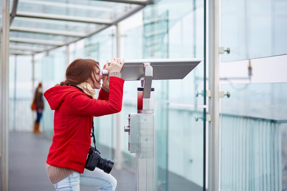 Cheerful young tourist using telescope on the Montparnasse tower observation deck in Paris