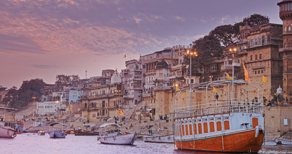 Varanasi, India. General View From Pleasure Boat on Chausathi Ghat. Purple Sunset Sky At Evening . Many Boats Moored On Ganga River. Devotees Take A Holy Dip In Water From This Ghat.